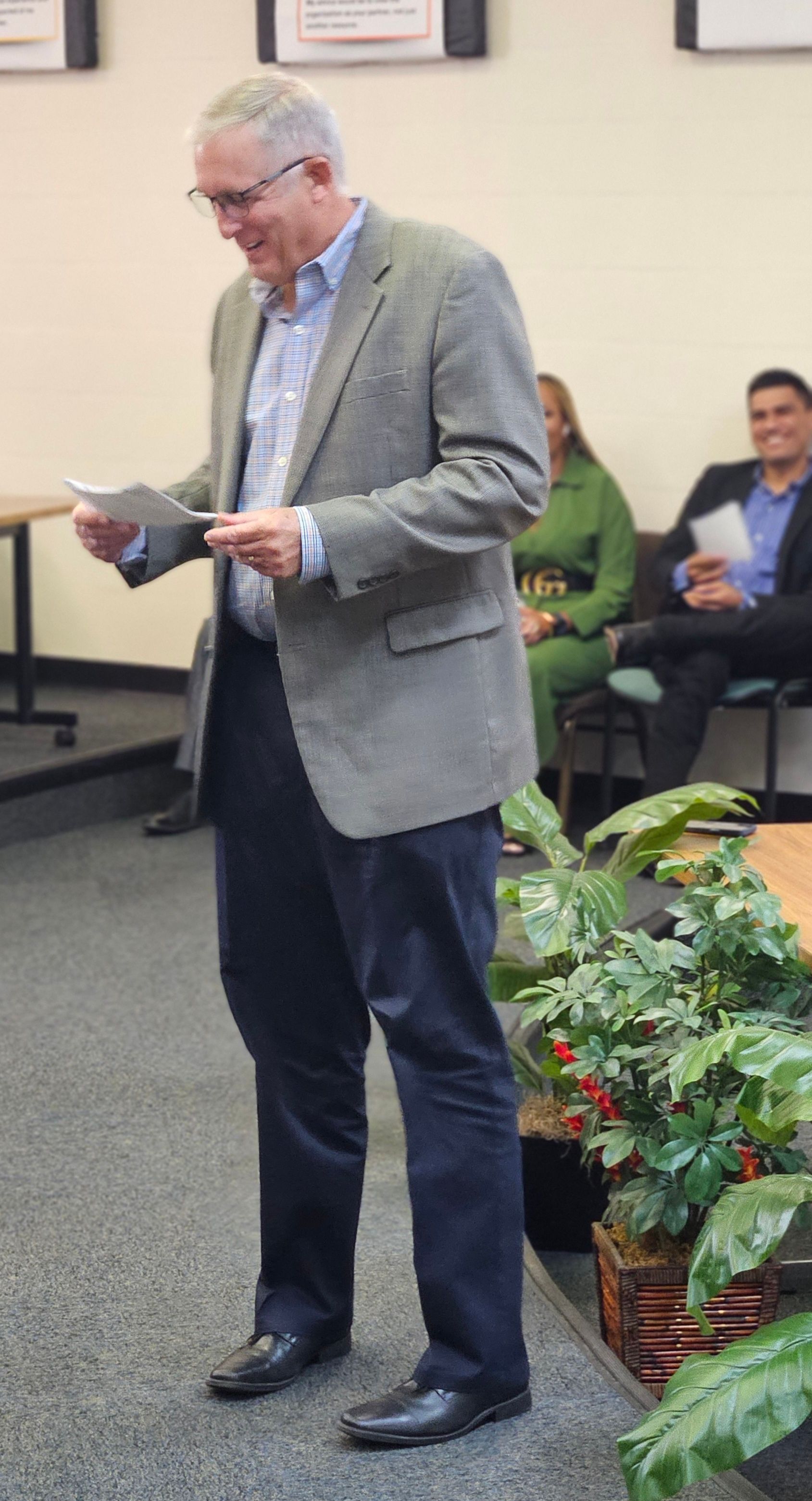 A man in a suit is standing in a room holding a piece of paper.