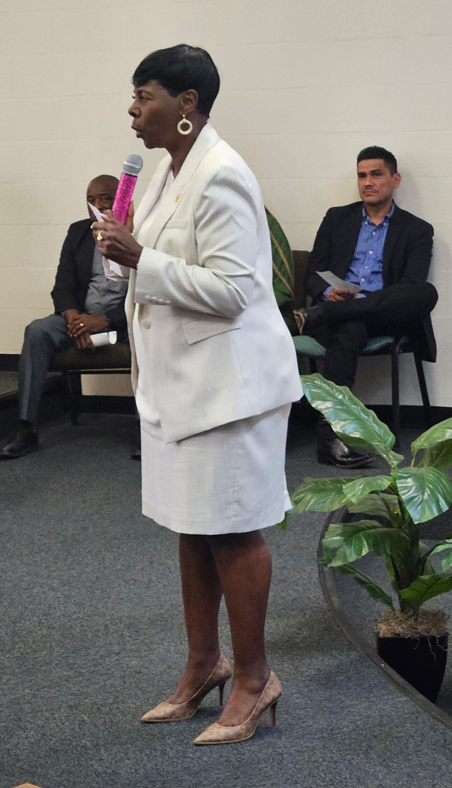 A woman in a white suit is speaking into a microphone