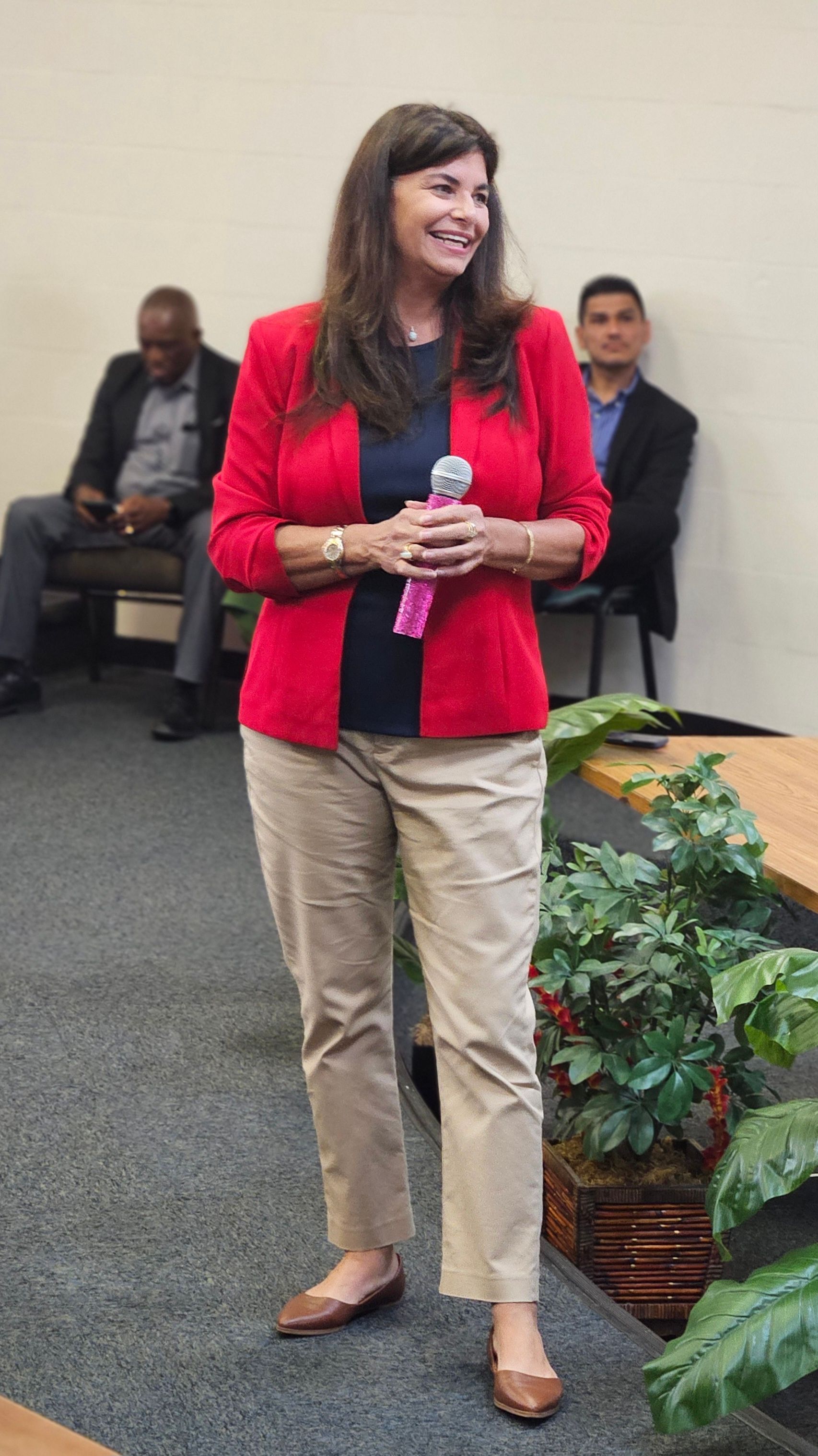 A woman in a red jacket is standing in front of a microphone.