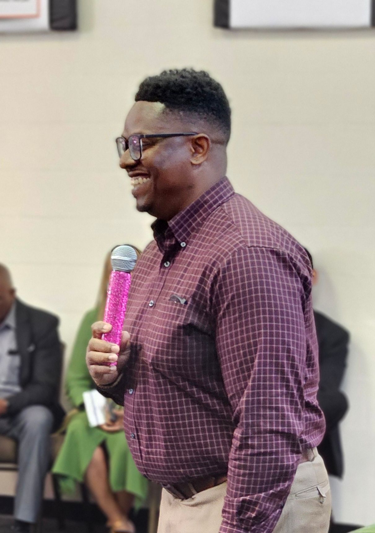 A man in a plaid shirt is holding a pink microphone.