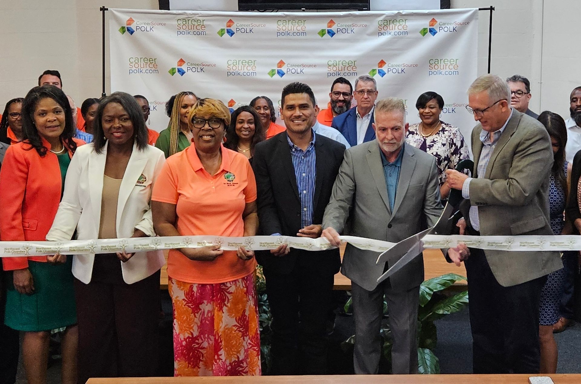 A group of people are standing around a table cutting a ribbon.