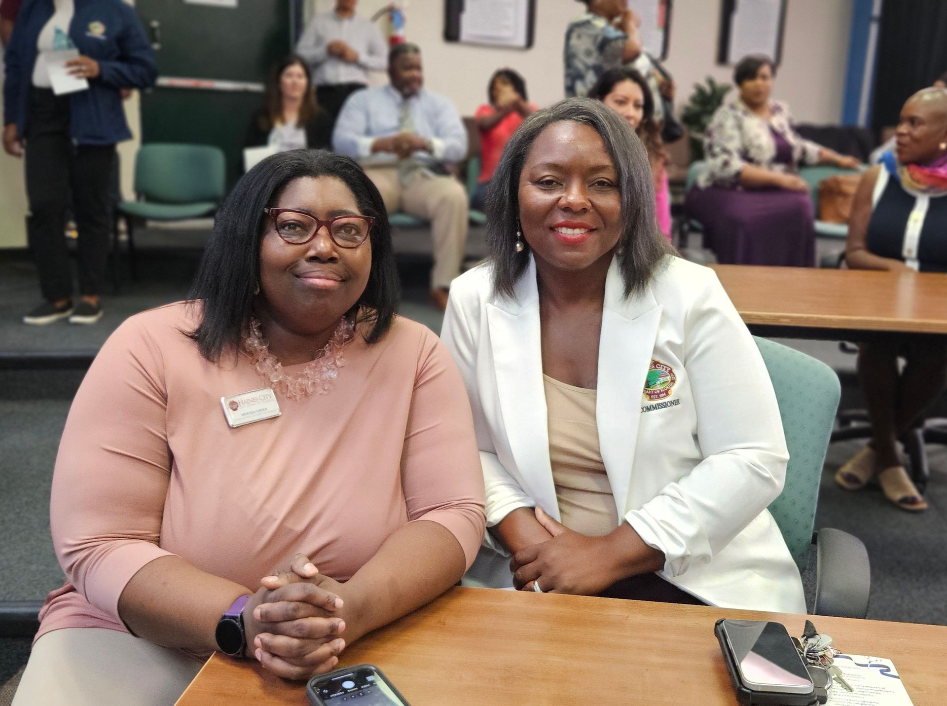 Two women are sitting at a table with their hands folded.