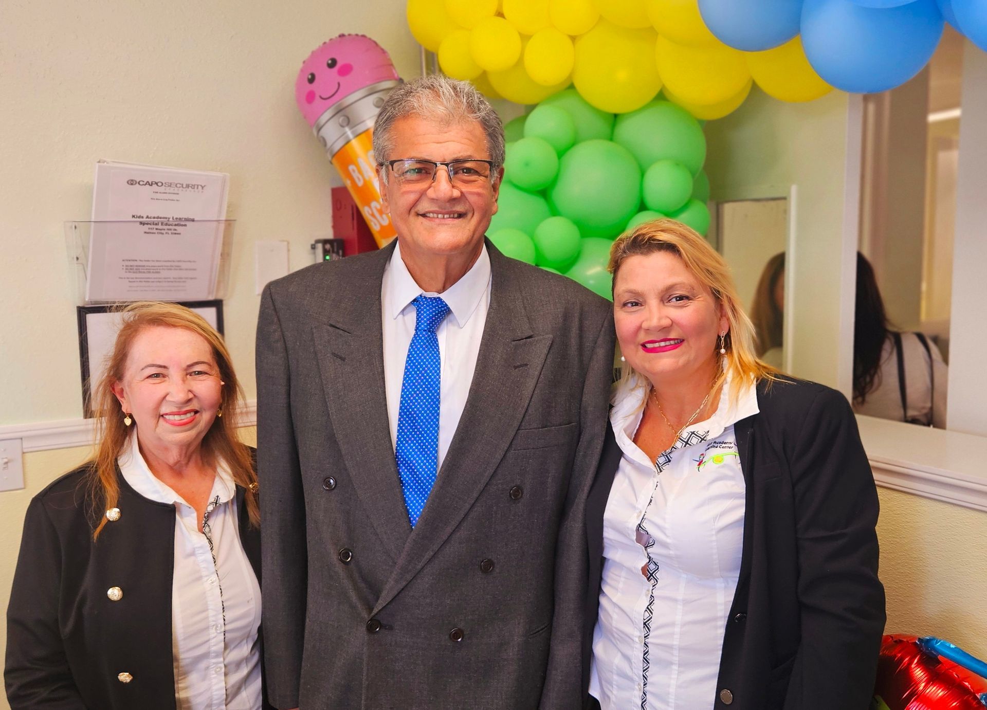 A man and two women are posing for a picture in front of balloons.