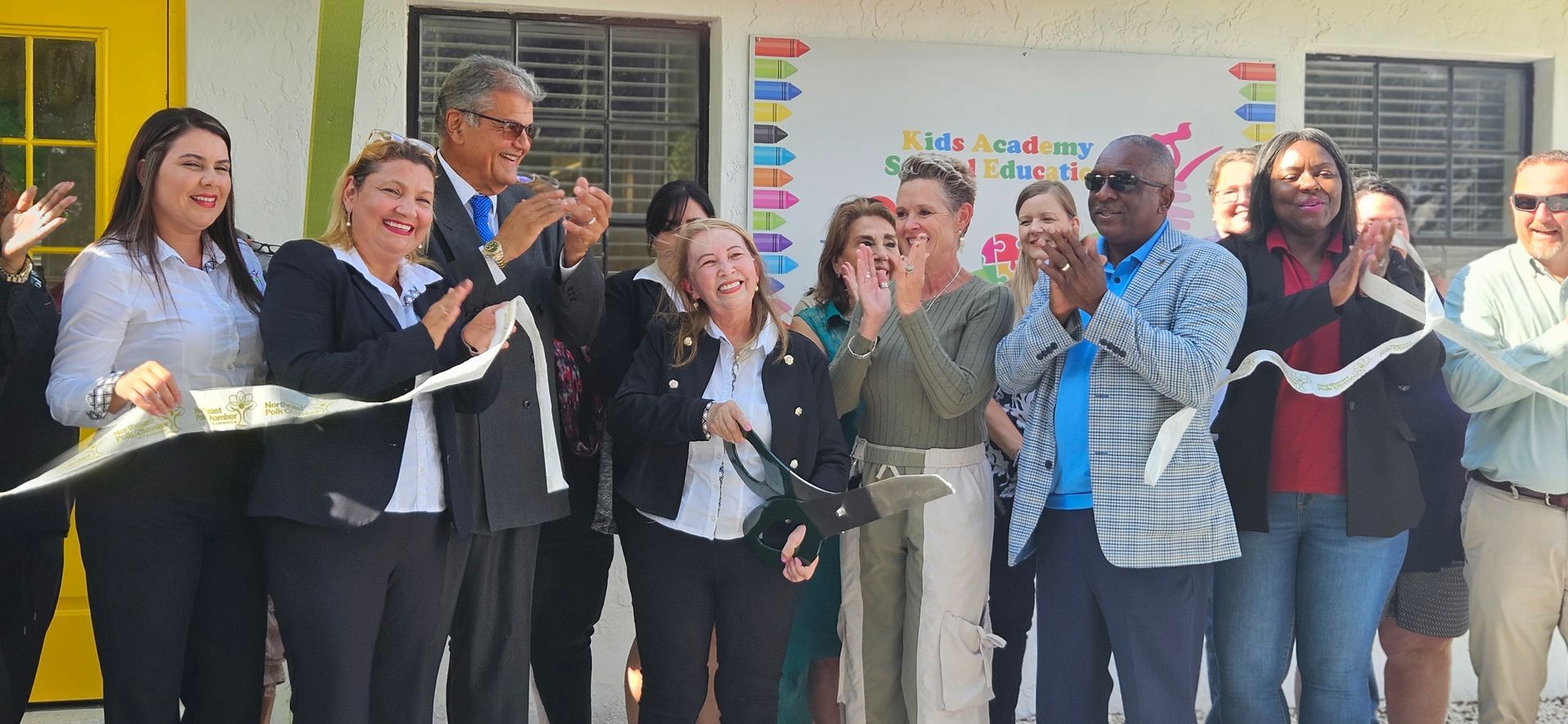 A group of people are standing in front of a building cutting a ribbon.