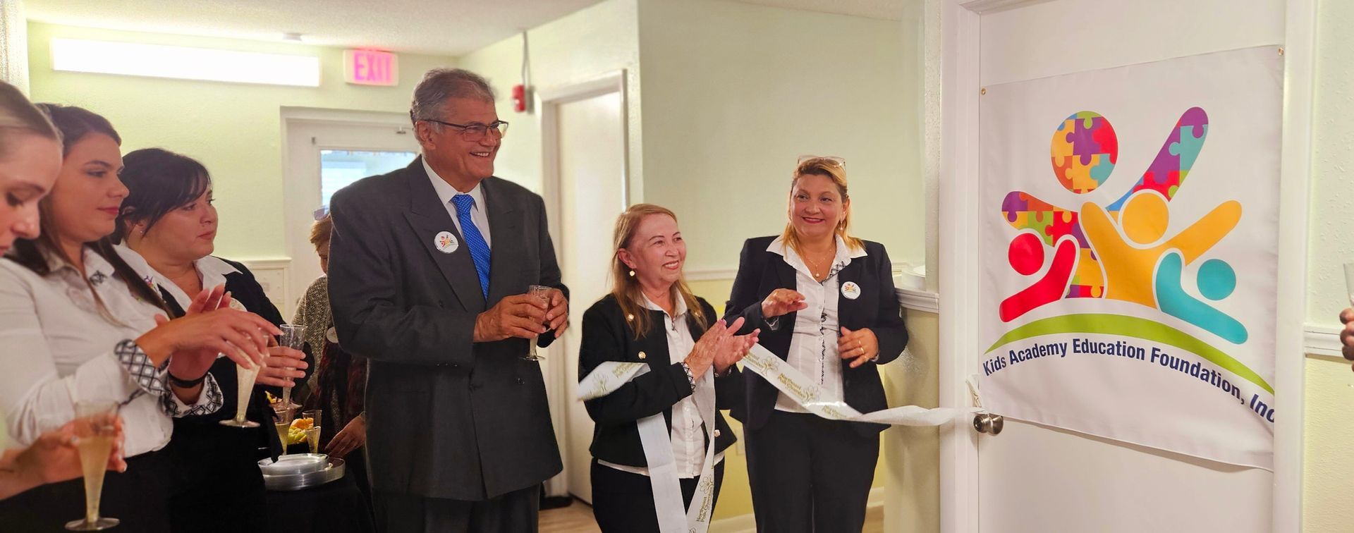 A group of people are standing around a door cutting a ribbon.