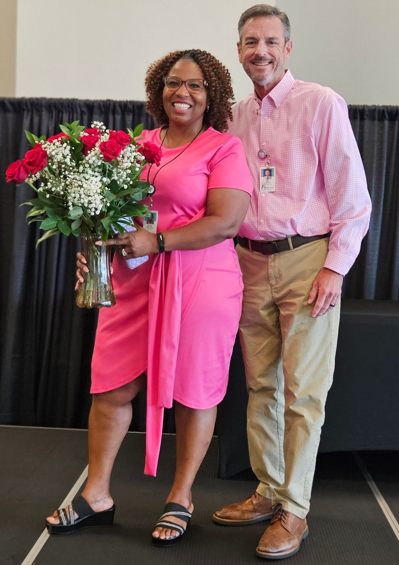 A woman in a pink dress is holding a vase of flowers next to a man.