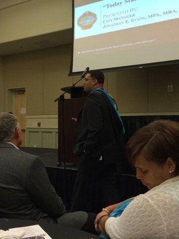 A man in a graduation cap and gown is giving a presentation to a group of people.