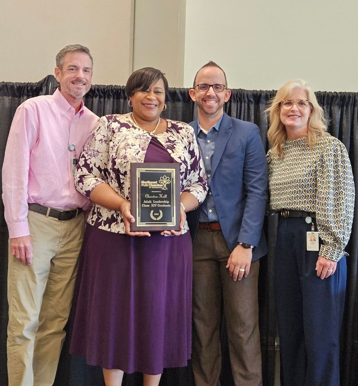 A woman in a purple dress is holding a framed award