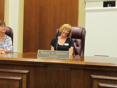 A woman is sitting at a desk with a sign that says peggy a quince justice