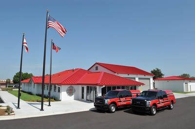 Three red trucks are parked in front of a building with a red roof.