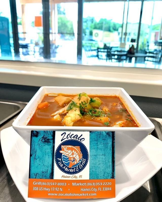 A bowl of soup is sitting on a table in front of a window.