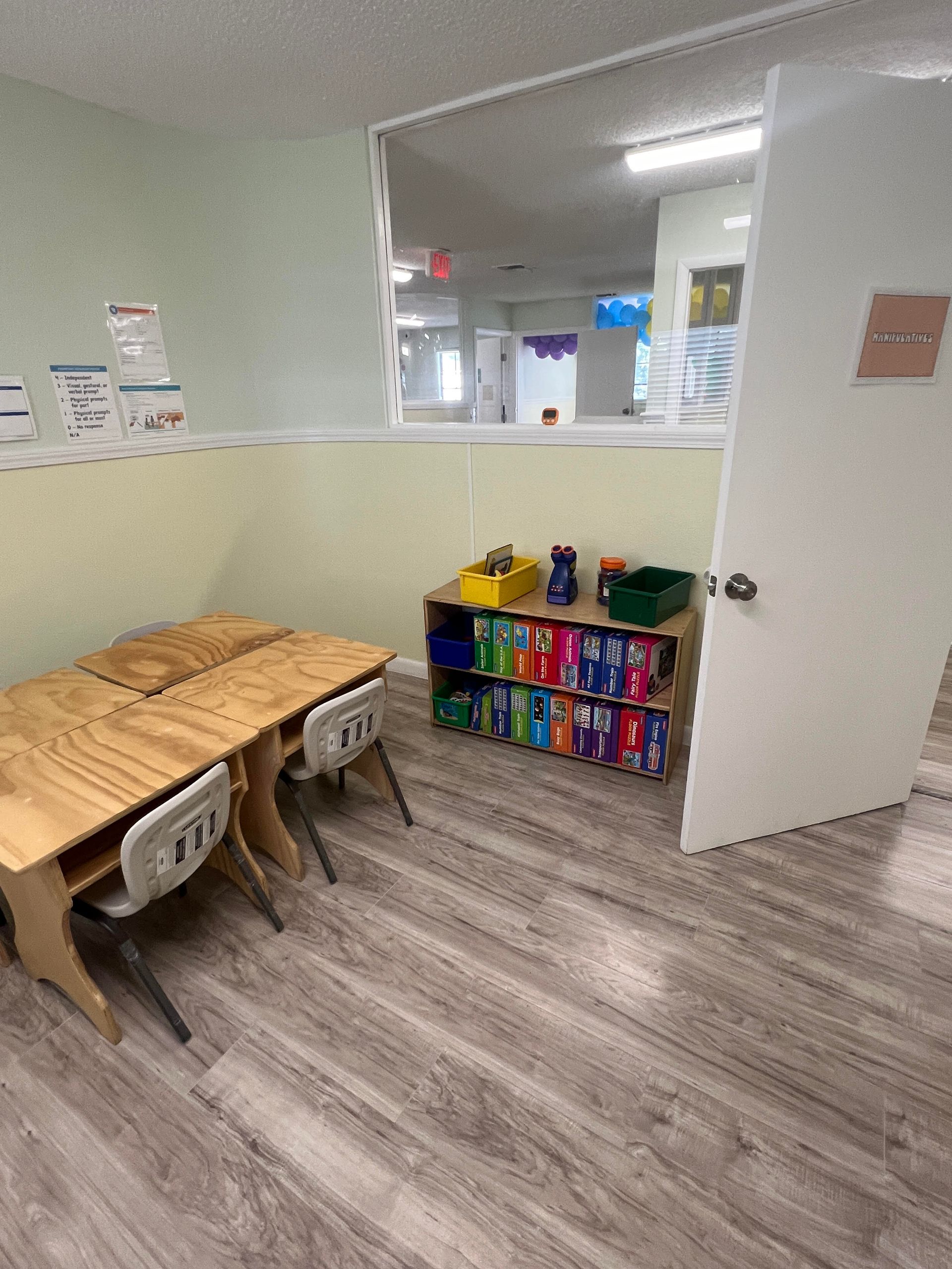 A classroom with wooden tables and chairs and a bookshelf filled with books.