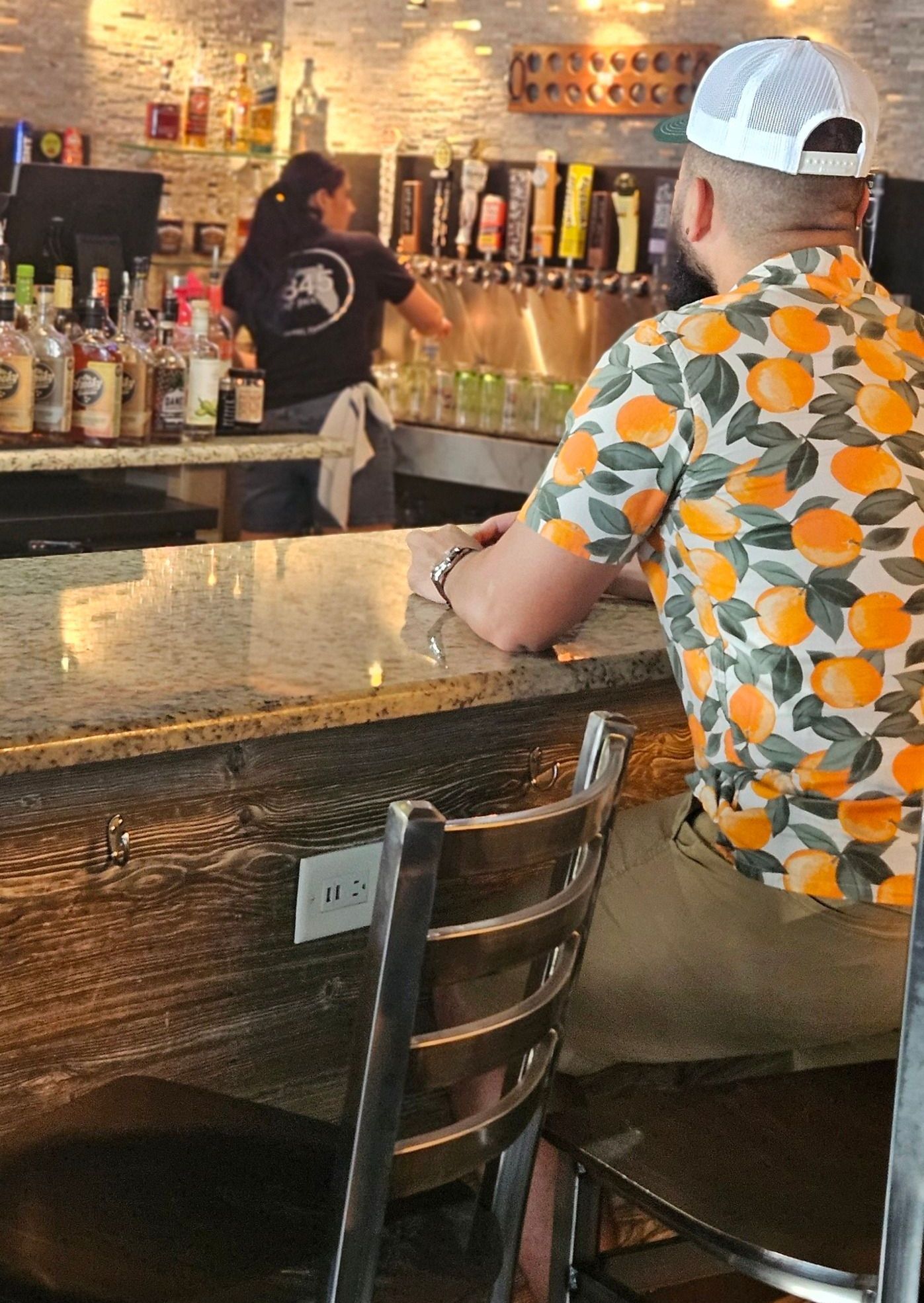 A man in an orange shirt is sitting at a bar