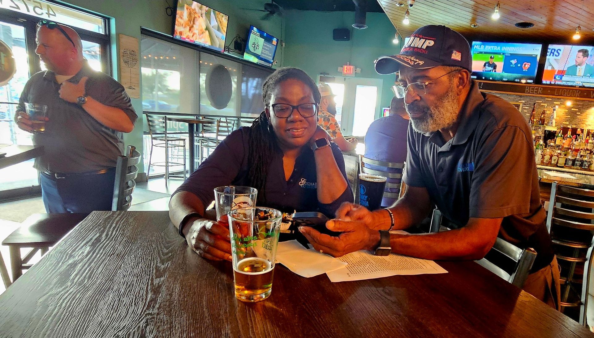 A man and a woman are sitting at a table in a restaurant looking at a cell phone.