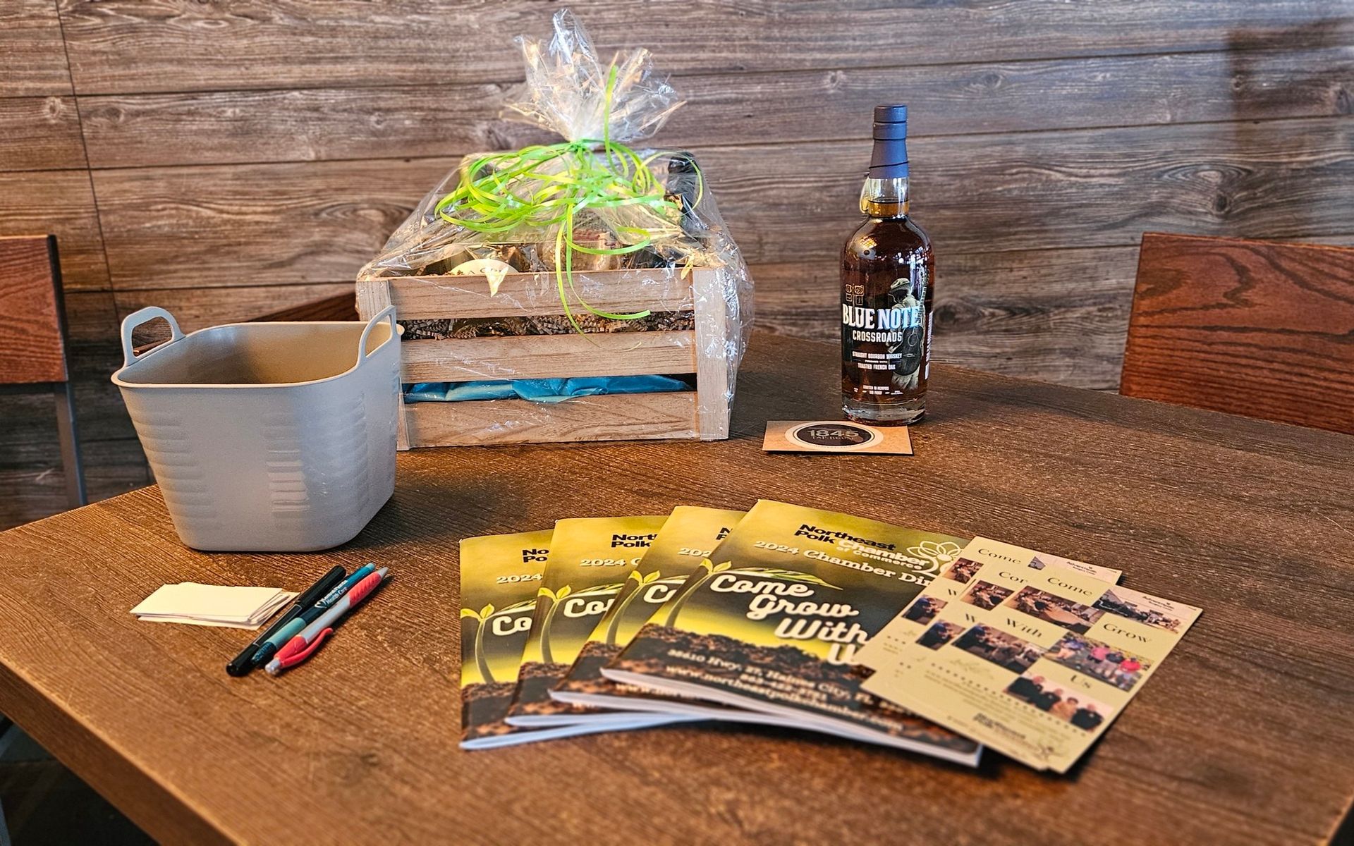 A table with a bottle of whiskey , magazines , and a basket on it.