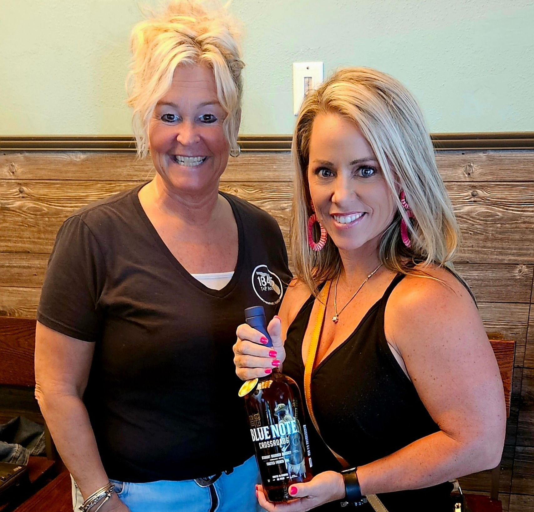 Two women standing next to each other holding a bottle of whiskey