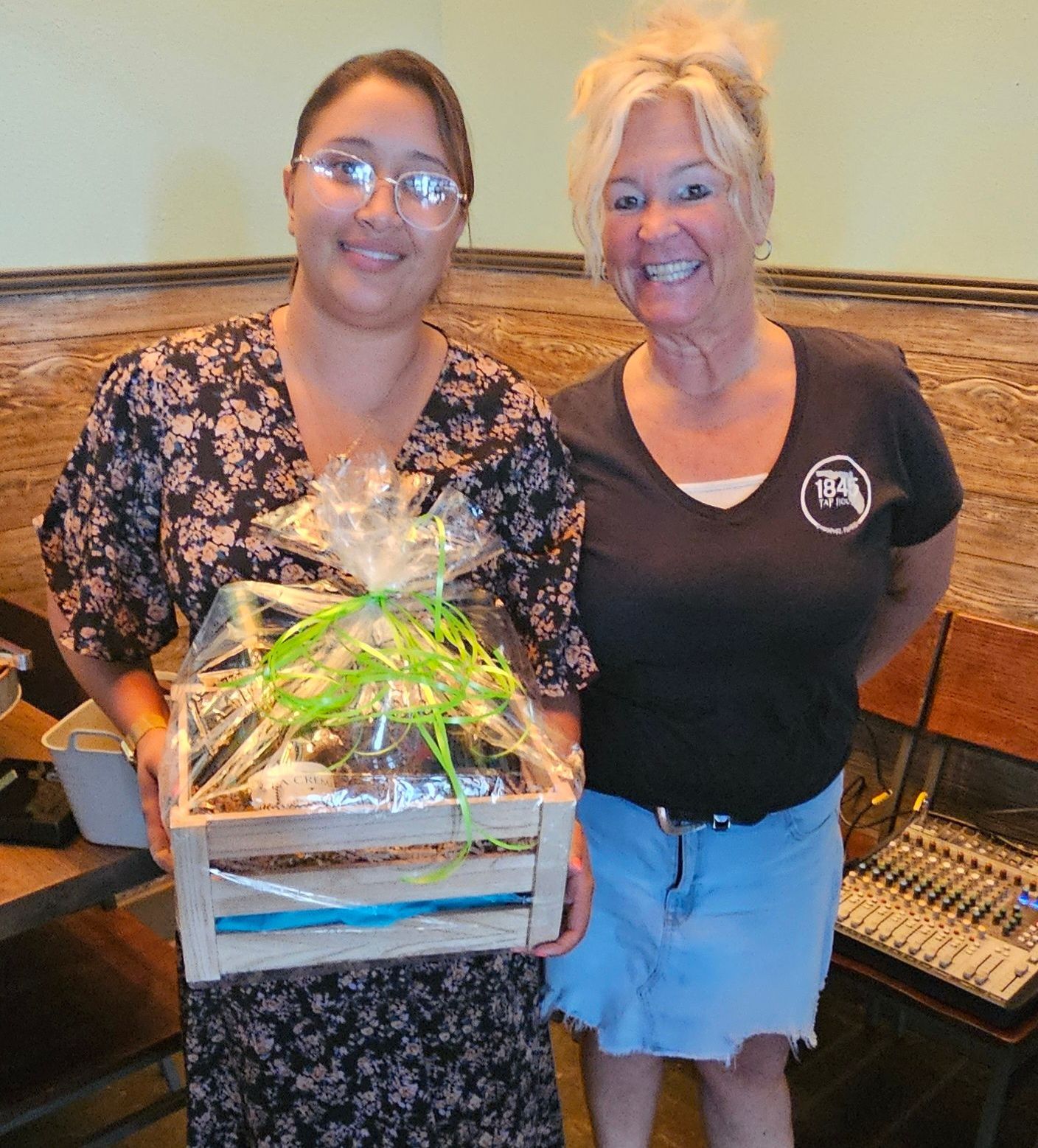 Two women standing next to each other holding a wooden crate