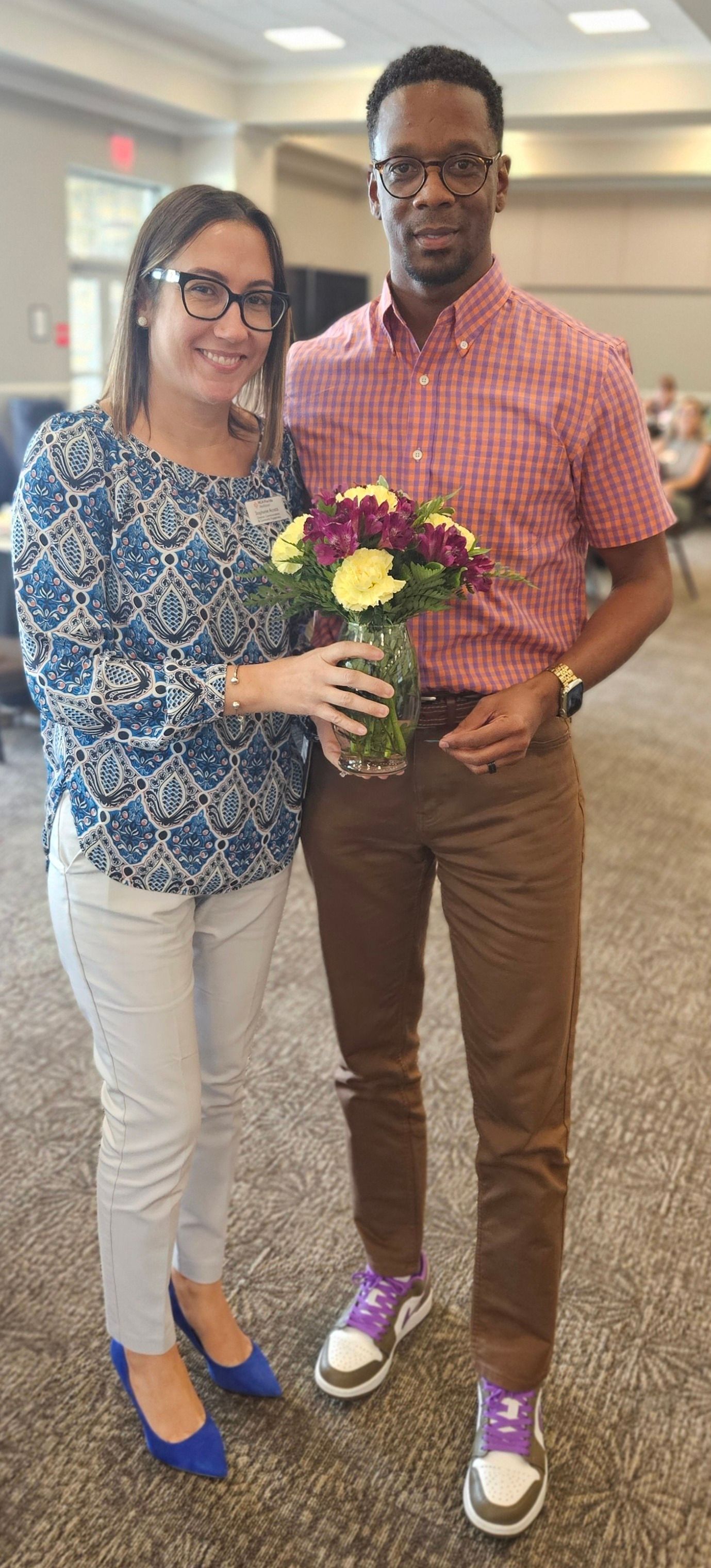 A man and a woman are standing next to each other holding a vase of flowers.