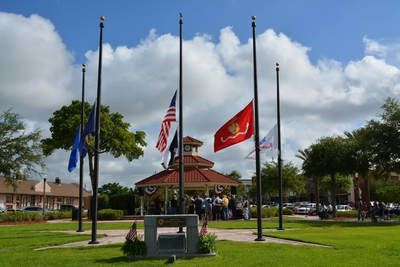 A group of people are standing in front of a gazebo with flags flying in the wind.