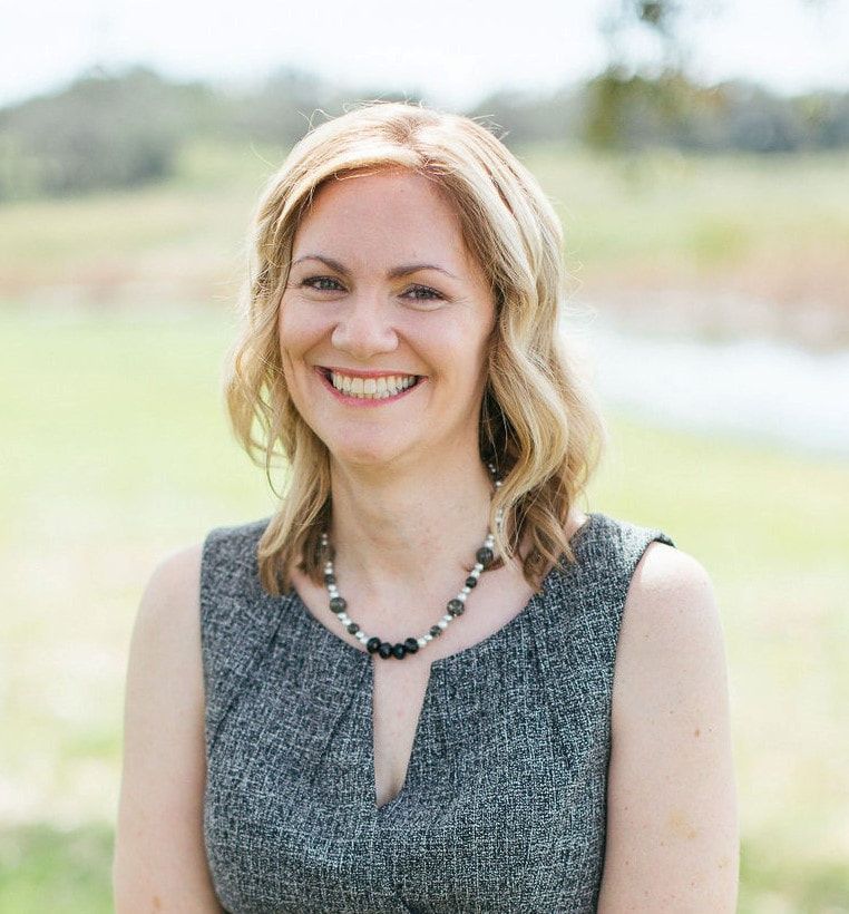 A woman wearing a gray dress and a necklace is smiling for the camera.