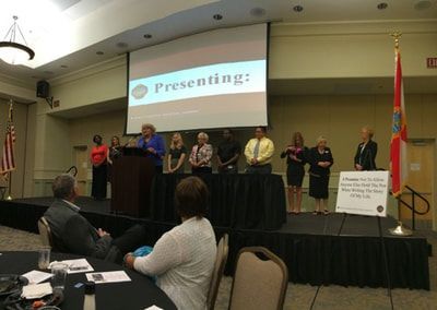 A group of people are standing on a stage in front of a screen that says presenting.