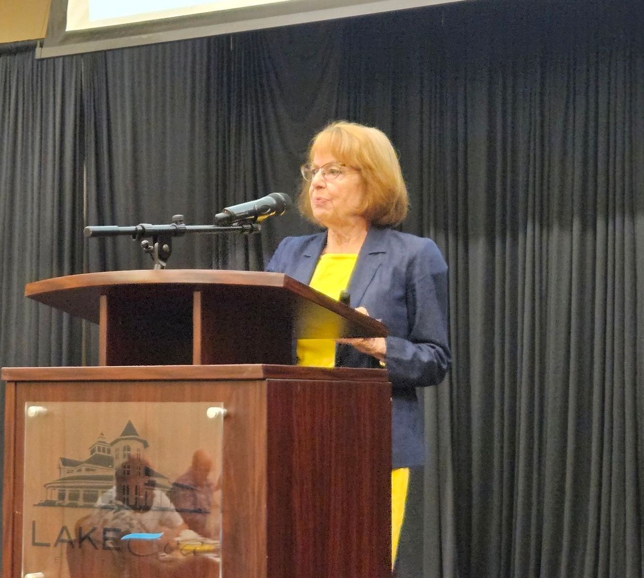 A woman stands at a podium that says lake on it