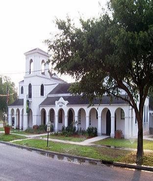 A large white building with arches and a tree in front of it.