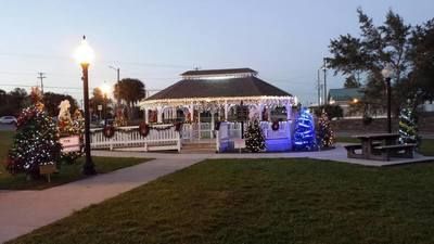 A gazebo is decorated with christmas lights and trees in a park.