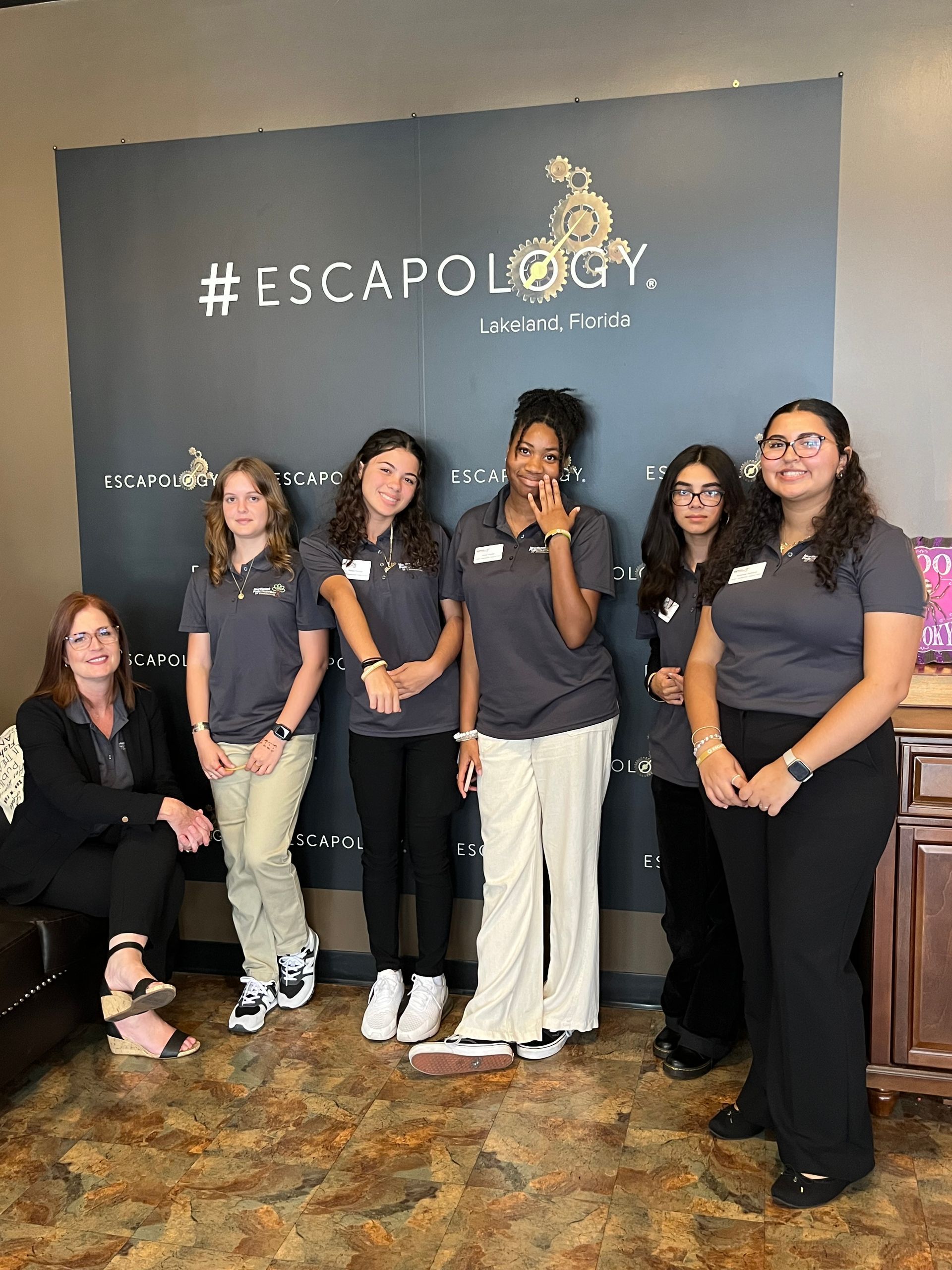 A group of young women are posing for a picture in front of a wall that says escapology.