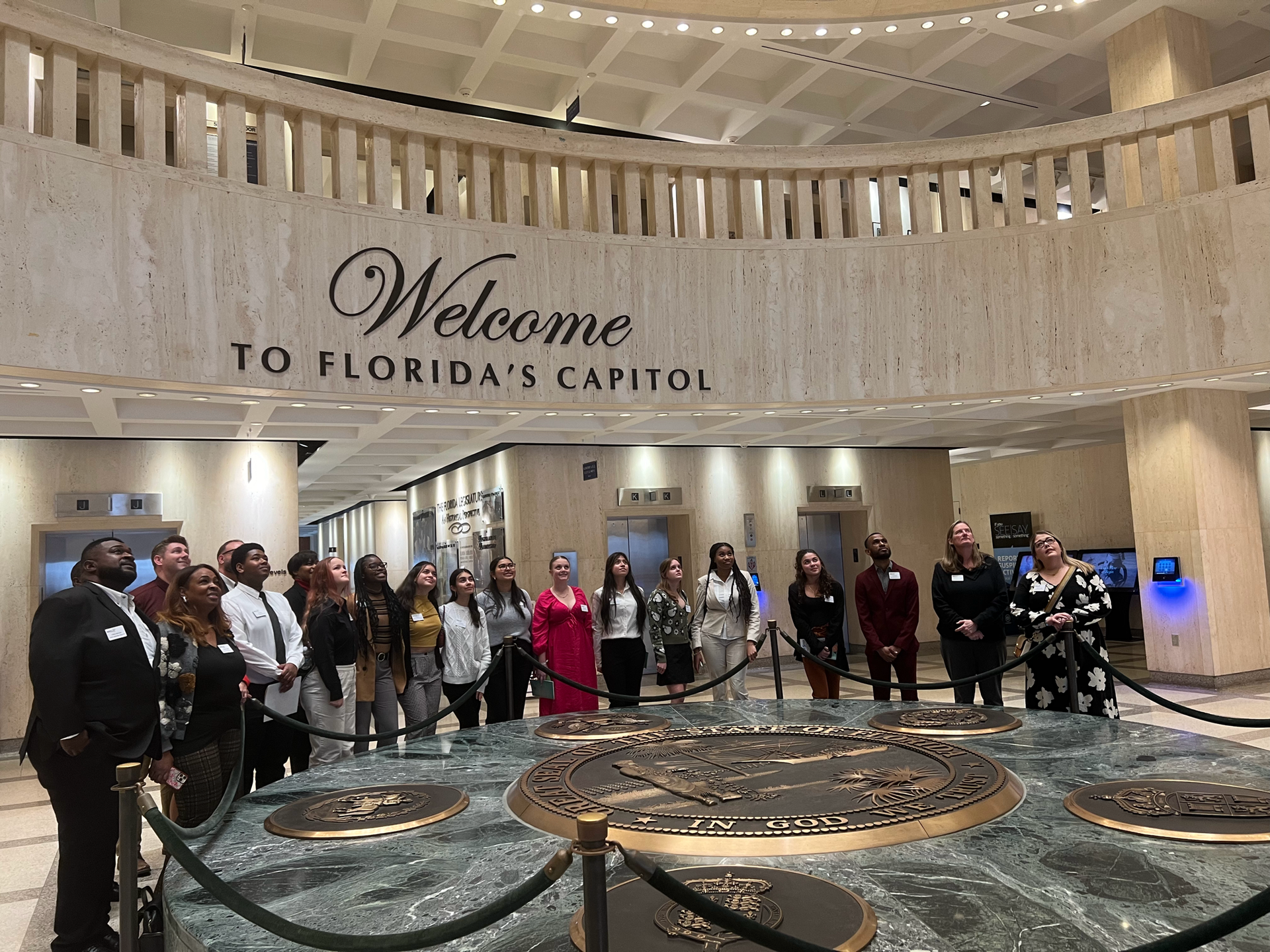 A group of people are standing in front of a sign that says welcome to florida 's capitol.