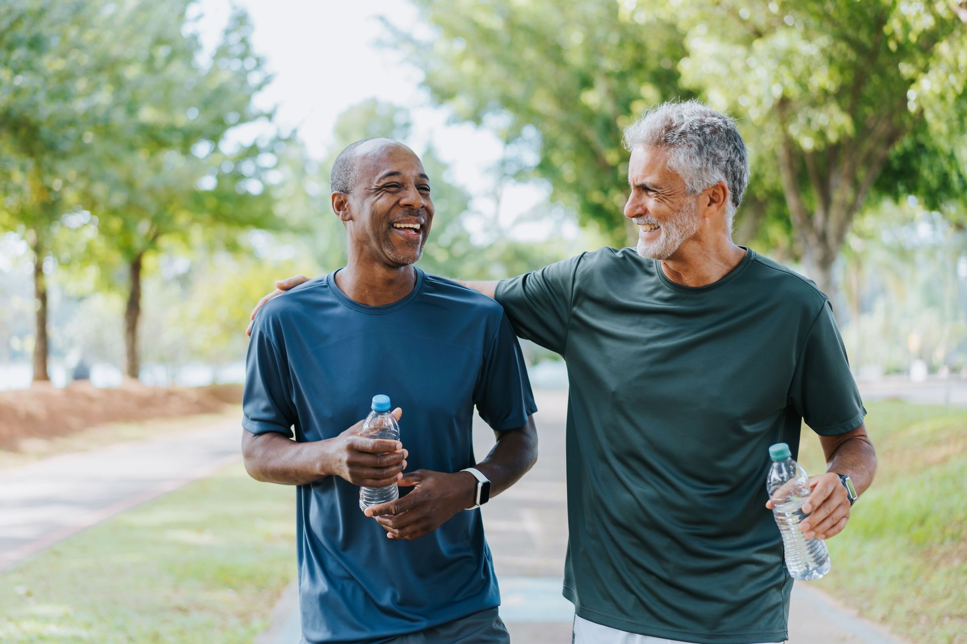 Two men are walking down a path in a park holding water bottles.