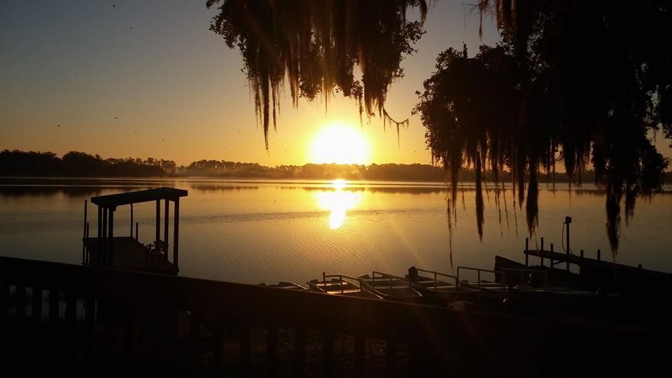 The sun is setting over a lake with a dock in the foreground.