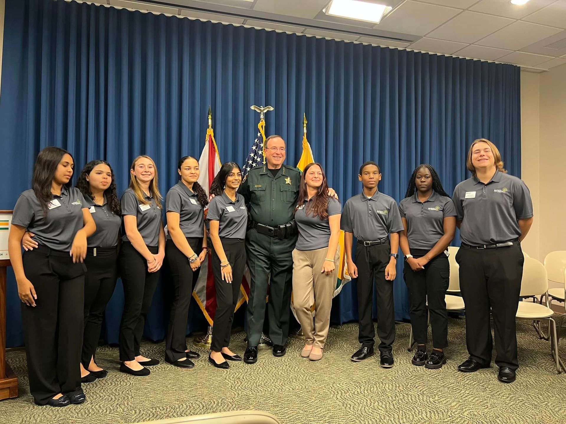 A group of people are posing for a picture with a police officer in a room.