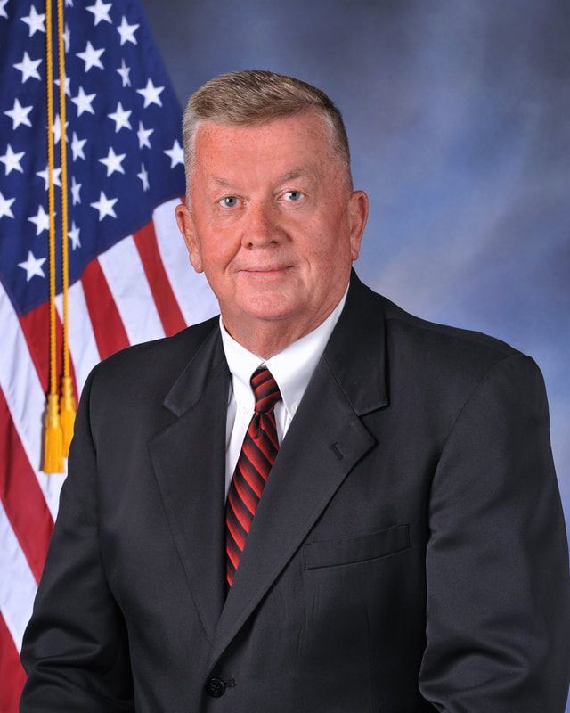 A man in a suit and tie stands in front of an american flag