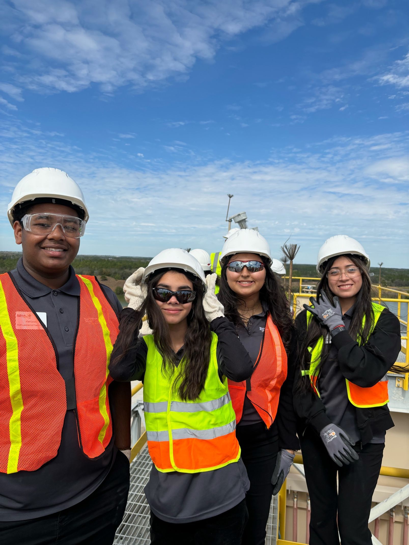 A group of young people wearing hard hats and safety vests are posing for a picture.