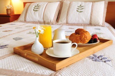 A wooden tray with breakfast on it is on a bed.