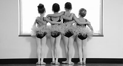 A group of young ballerinas are standing next to each other in front of a window