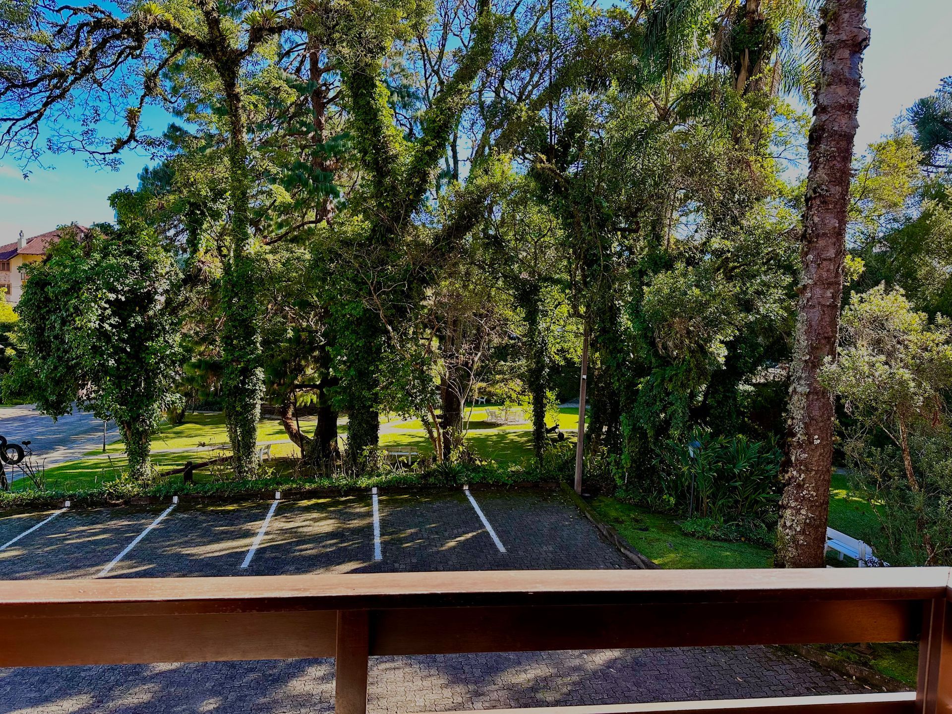 Vista de um estacionamento a partir de uma varanda com árvores ao fundo.