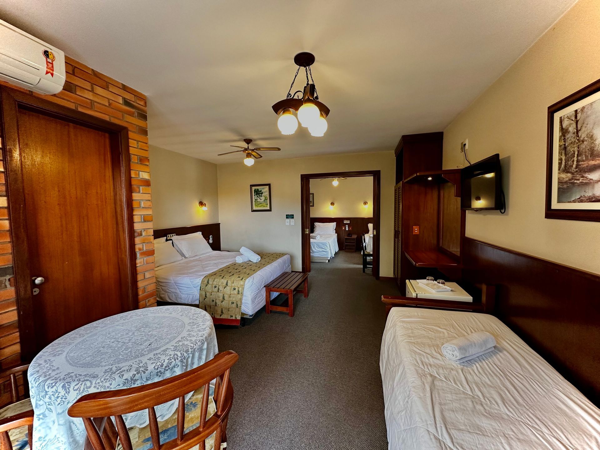 Um quarto de hotel com três camas, mesa e cadeiras.