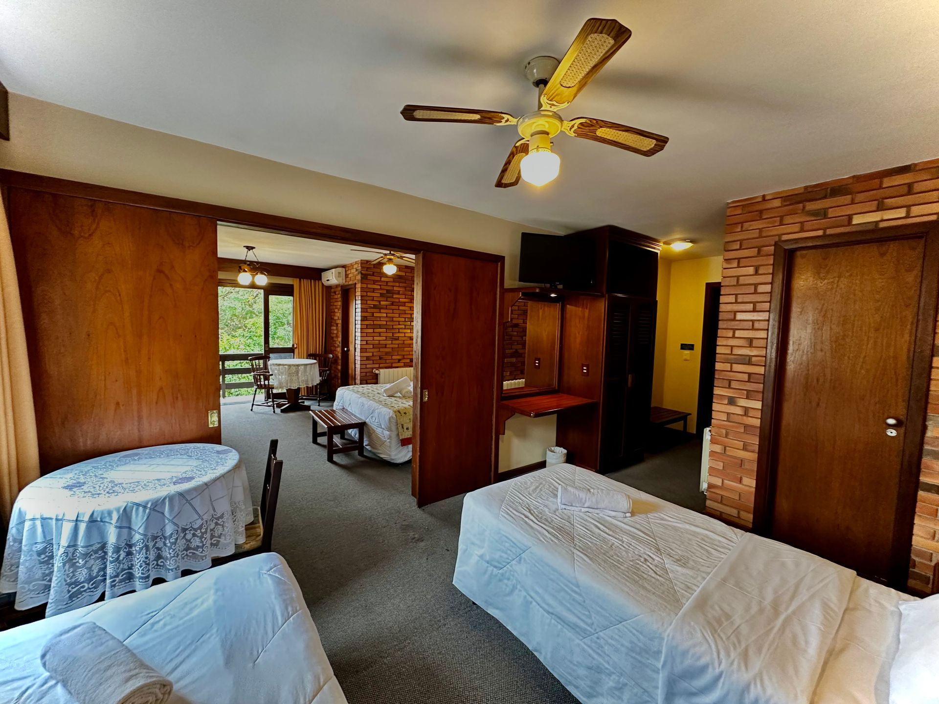 Um quarto de hotel com duas camas, uma mesa e um ventilador de teto.