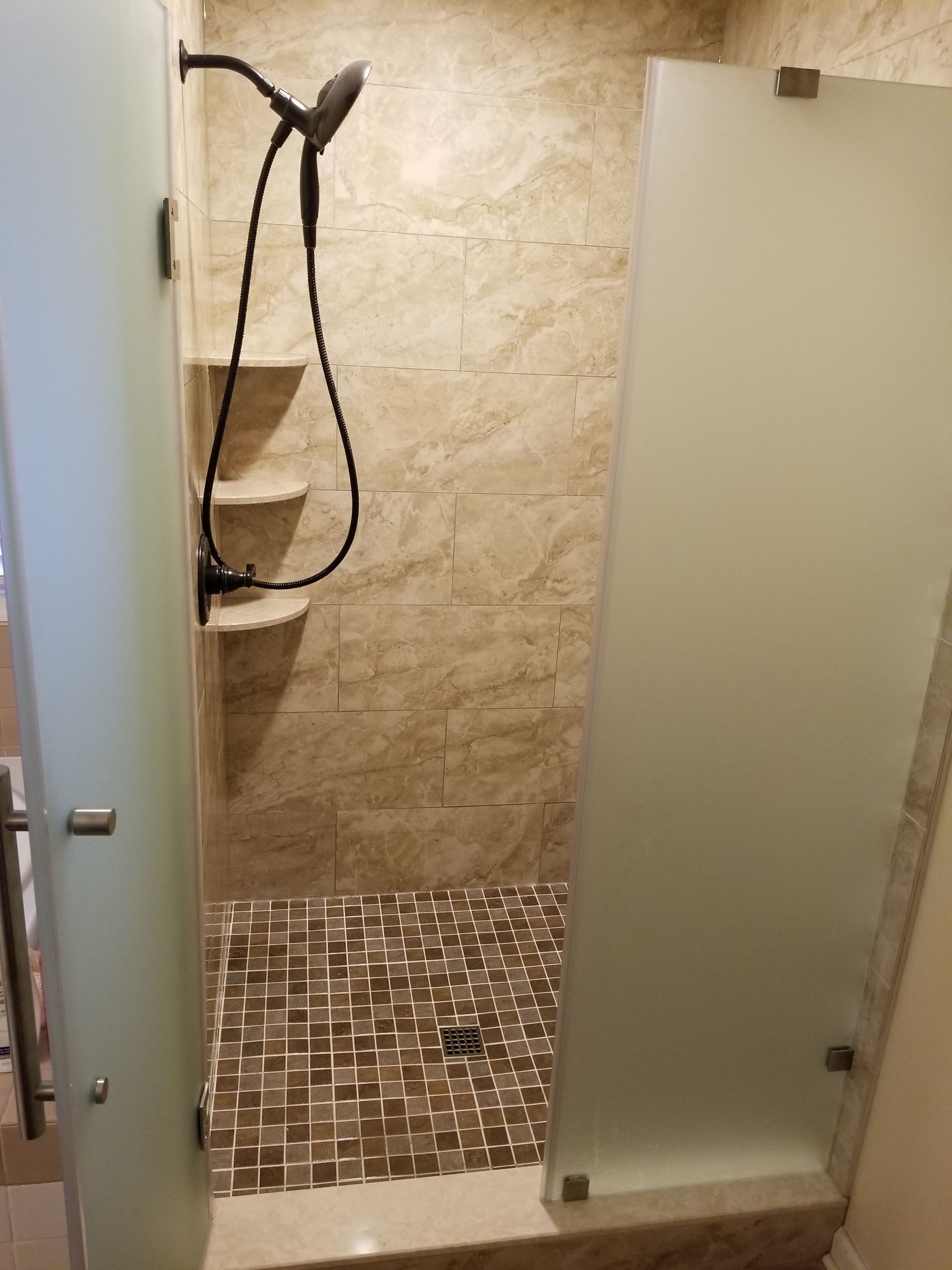 A bathroom with a walk in shower with a glass door and a shower head.
