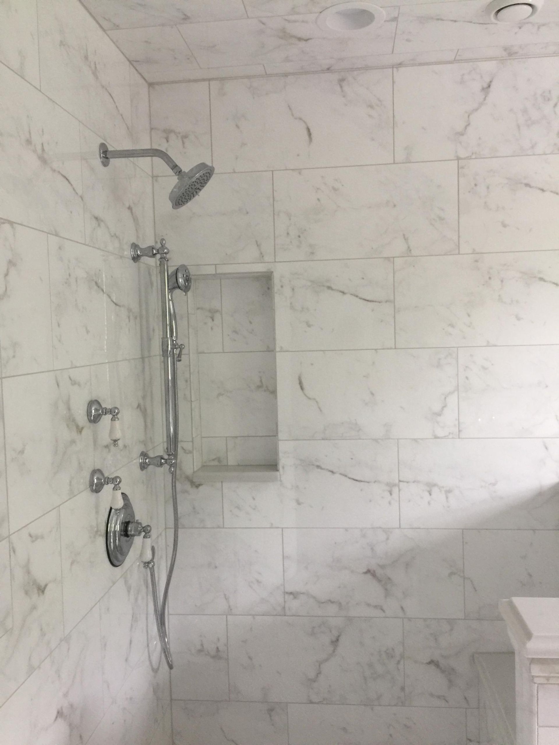 A bathroom with marble tiles and a shower head.