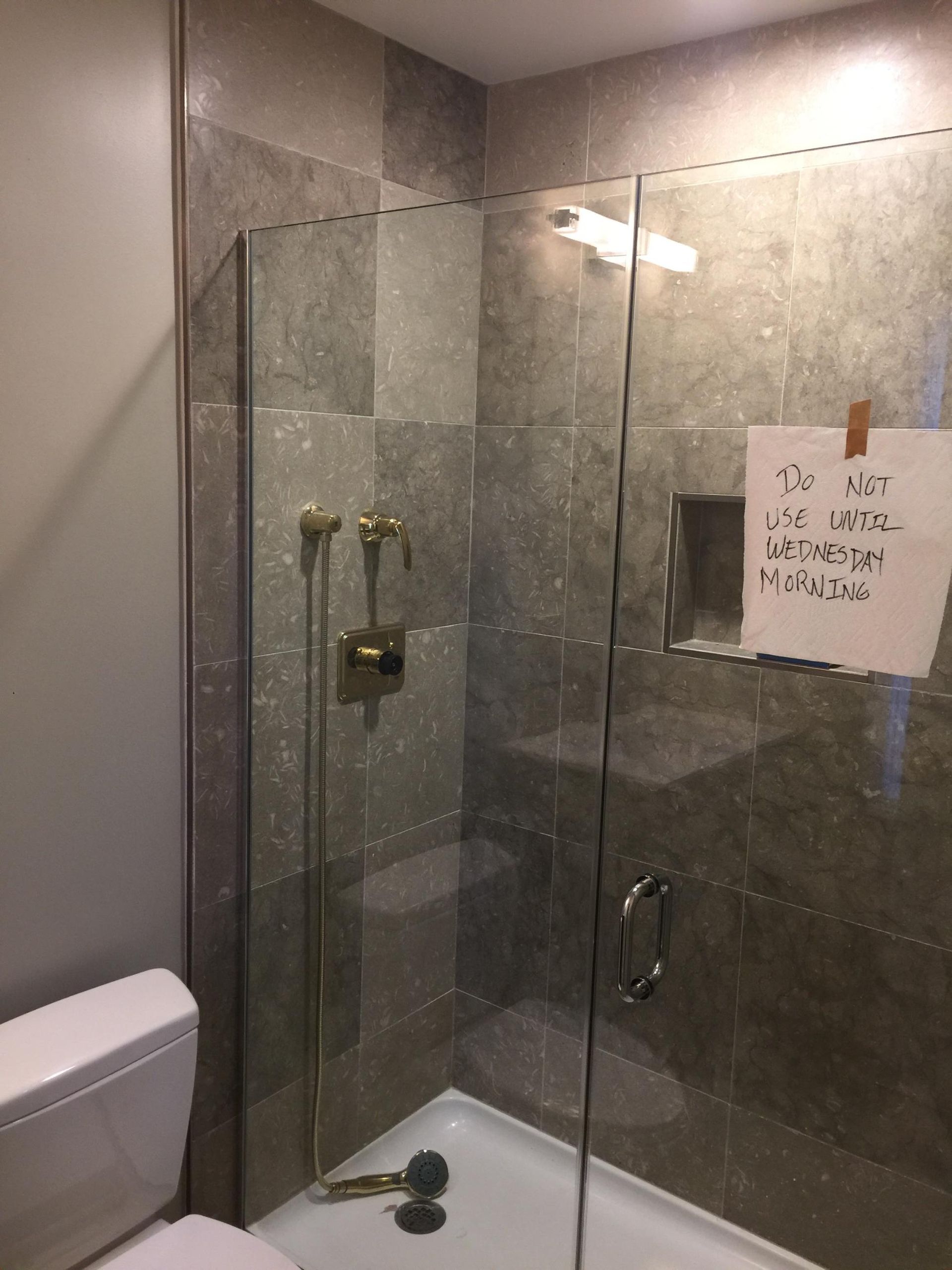 A bathroom with a toilet and a walk in shower with a sign taped to the wall.