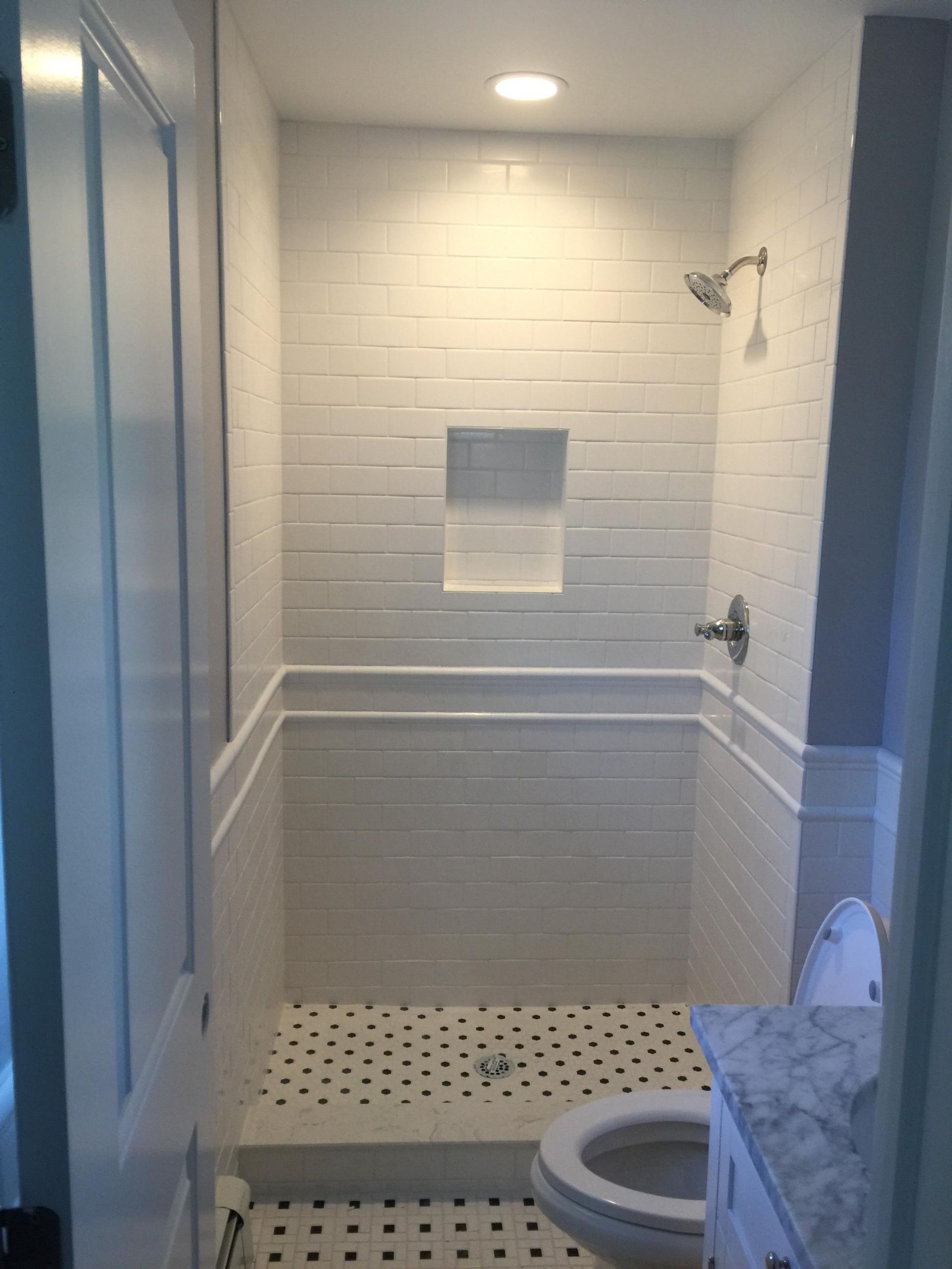 A bathroom with white tiles , a toilet , and a shower.