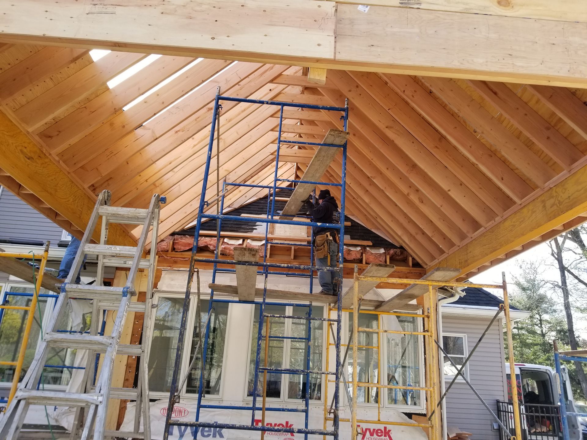 A man is standing on a scaffolding in front of a house under construction.