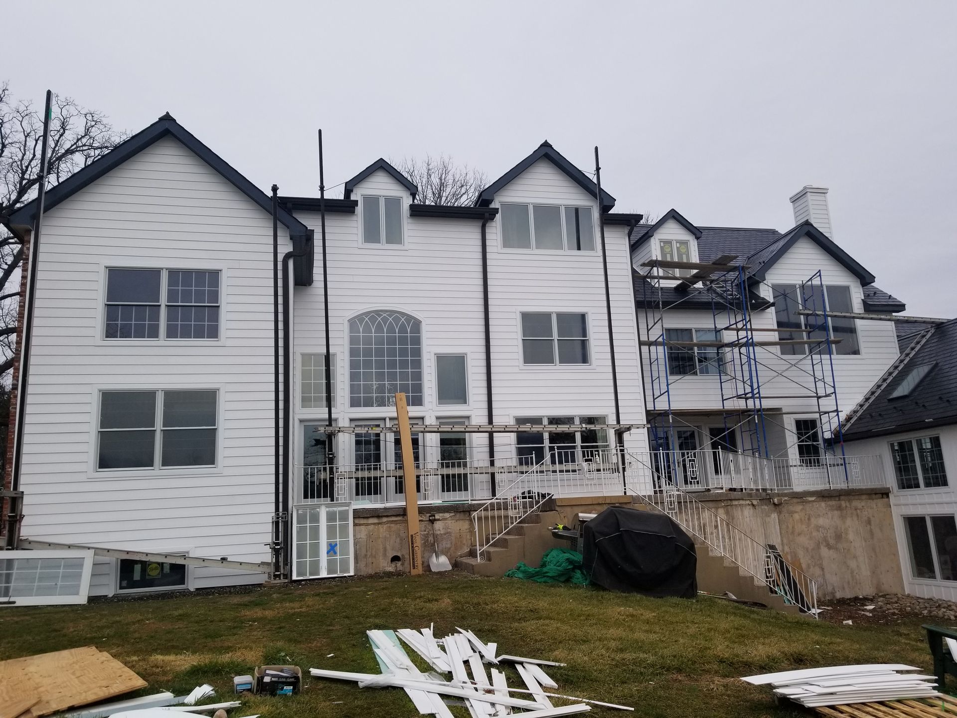 A large white house with a black roof is under construction.