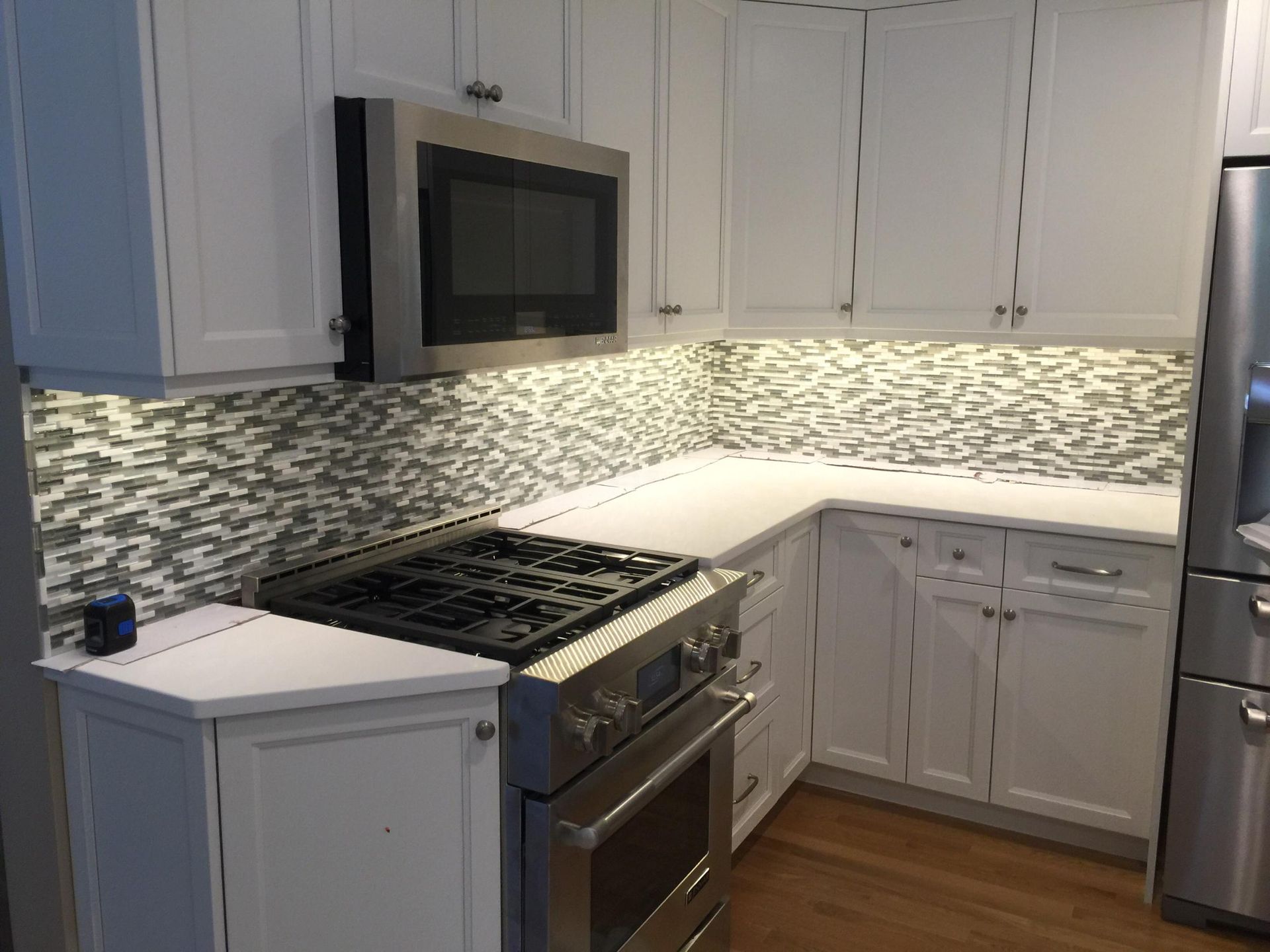 A kitchen with white cabinets , stainless steel appliances , a stove , microwave and refrigerator.
