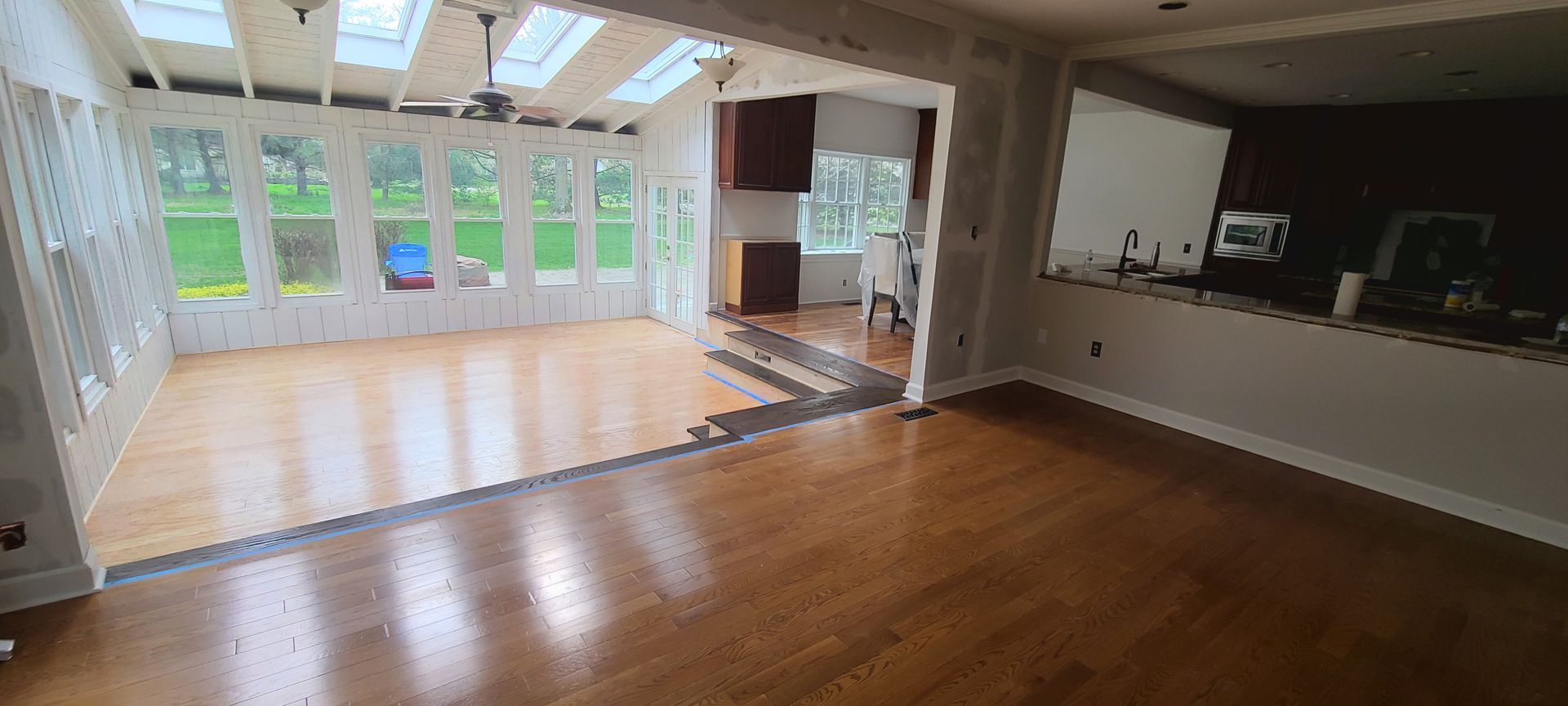 An empty room with hardwood floors and a kitchen in the background.