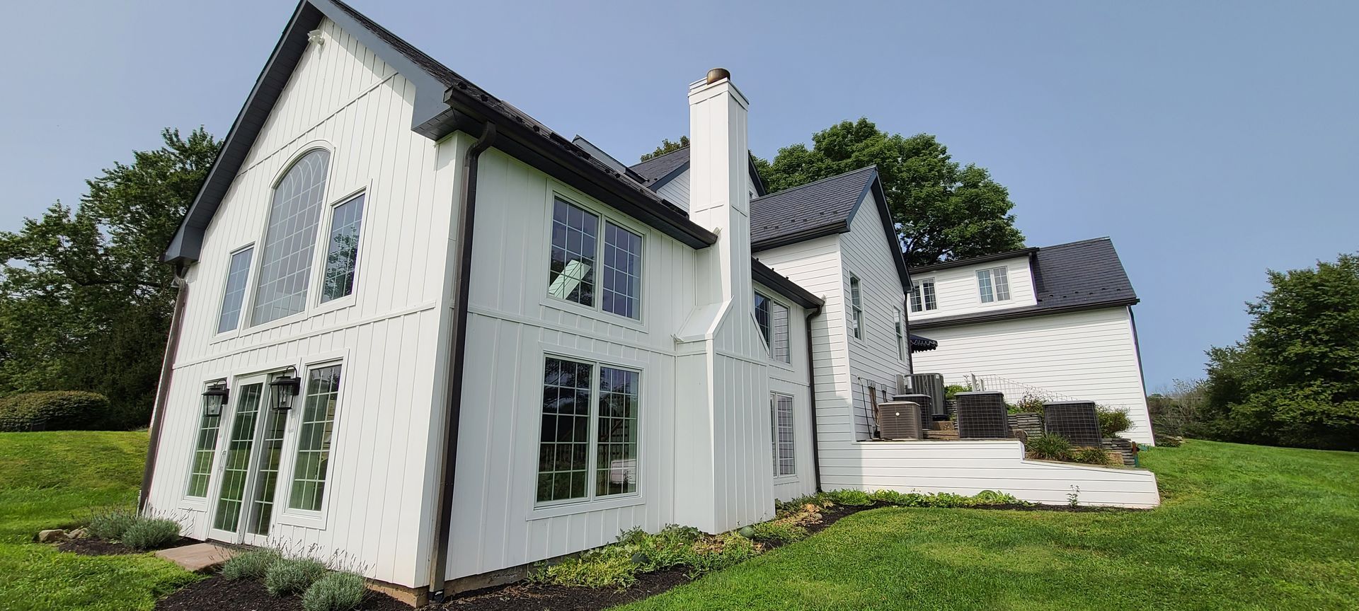 A large white house with a black roof is sitting on top of a lush green hill.