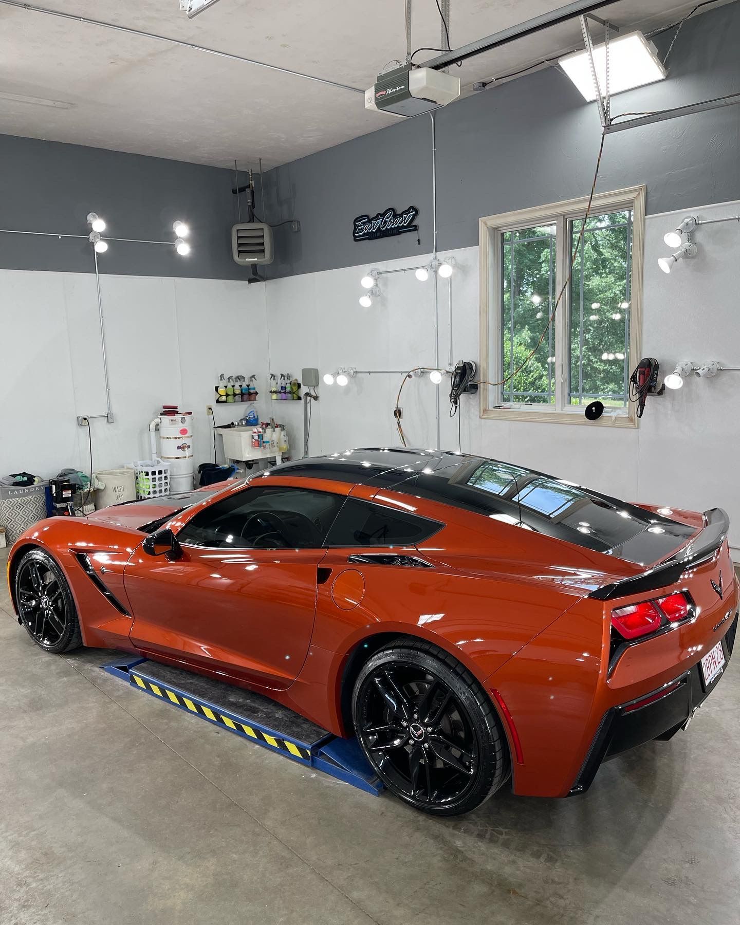 A red sports car is parked in a garage next to a window.